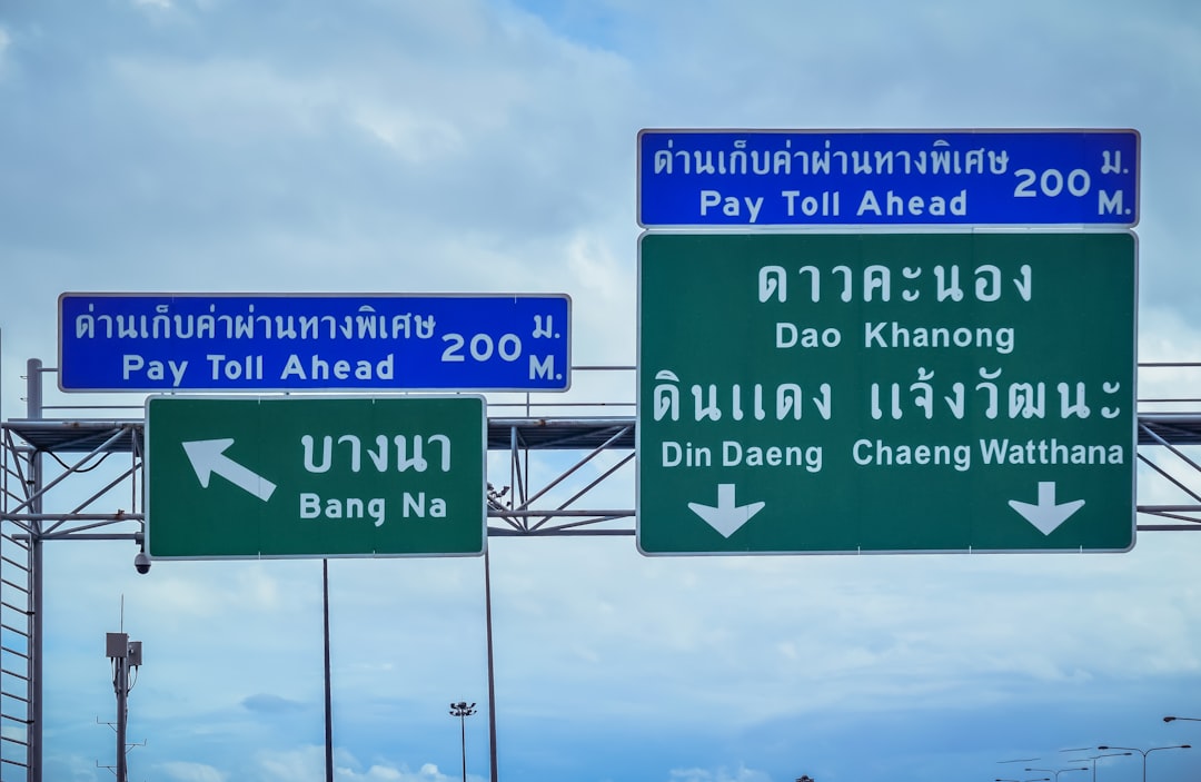 Thai highway signs showing toll booth ahead and directions to Bang Na, Dao Khanong, Din Daeng, and Chaeng Watthana districts