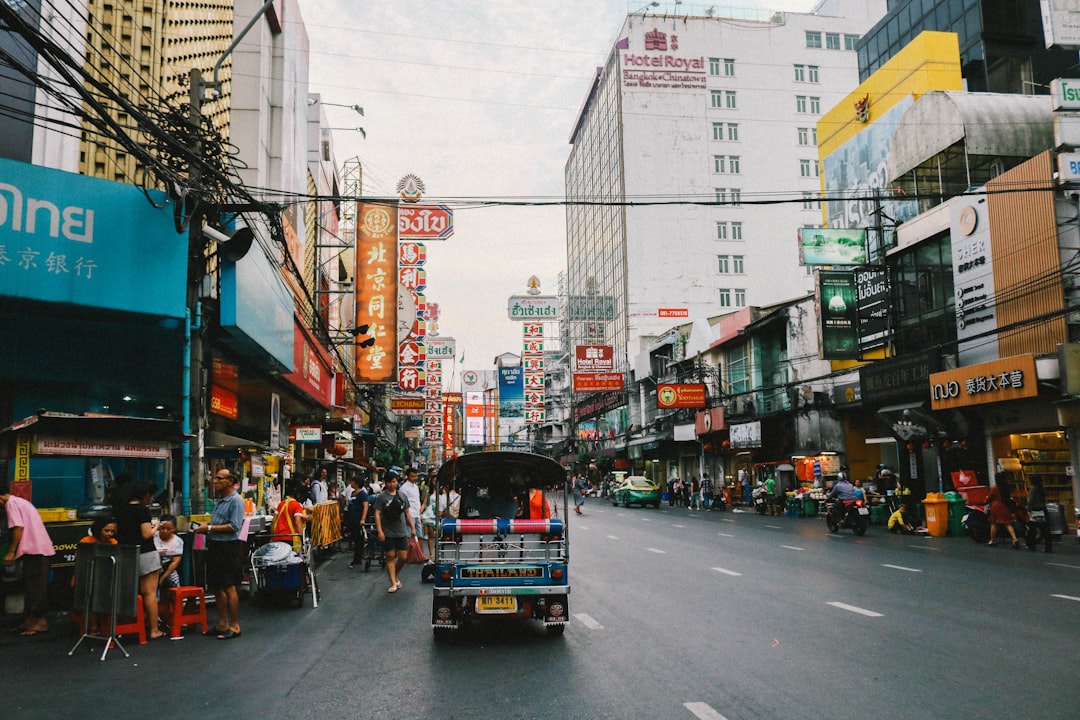 Busy Bangkok street scene with tuk-tuk, colorful neon signs, and crowded pedestrians in Chinatown
