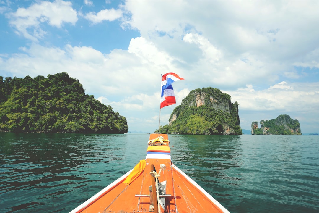 Traditional orange longtail boat with Thai flag heading toward limestone cliffs in turquoise waters