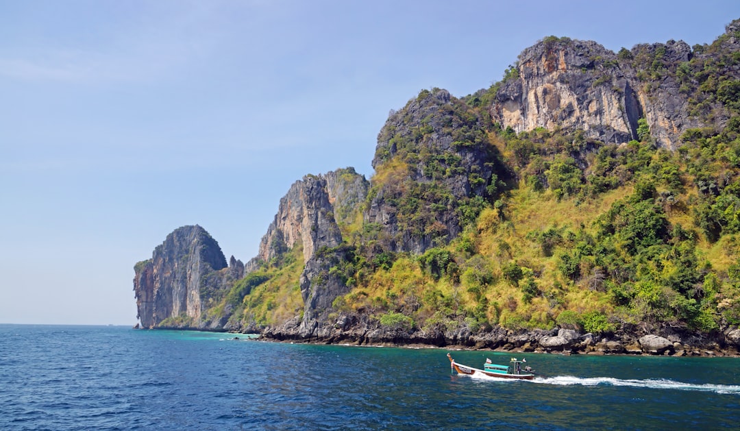 Limestone cliffs and tropical vegetation overlooking turquoise waters with a traditional longtail boat in Thailand