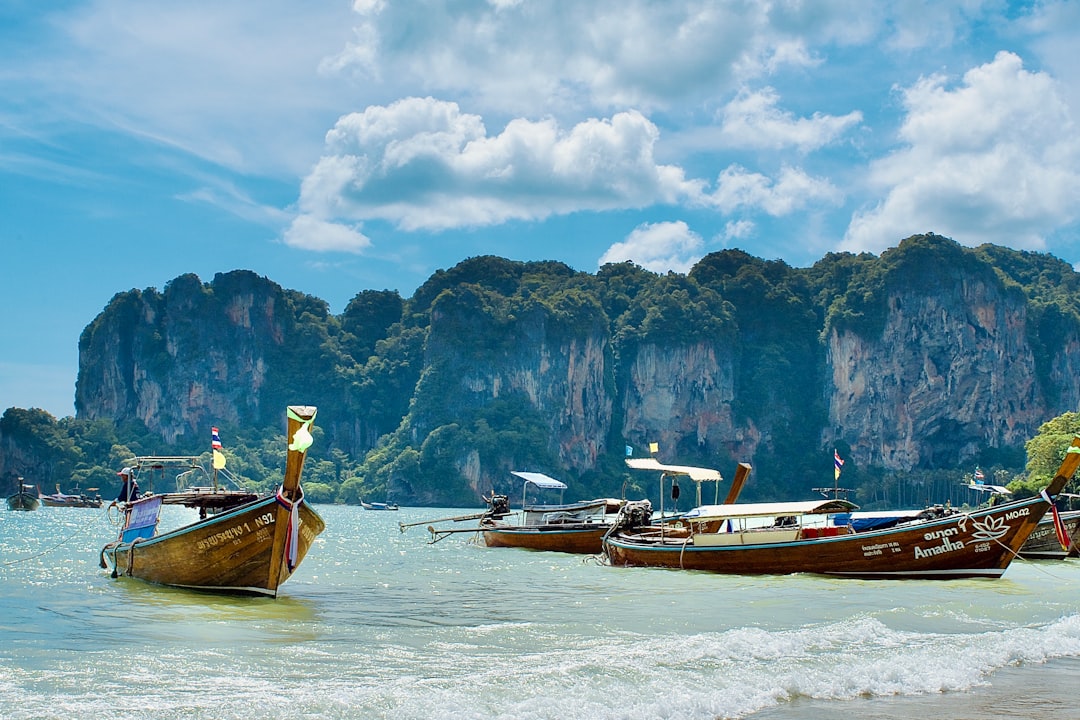 Traditional long-tail boats moored in turquoise waters near towering limestone cliffs in Thailand